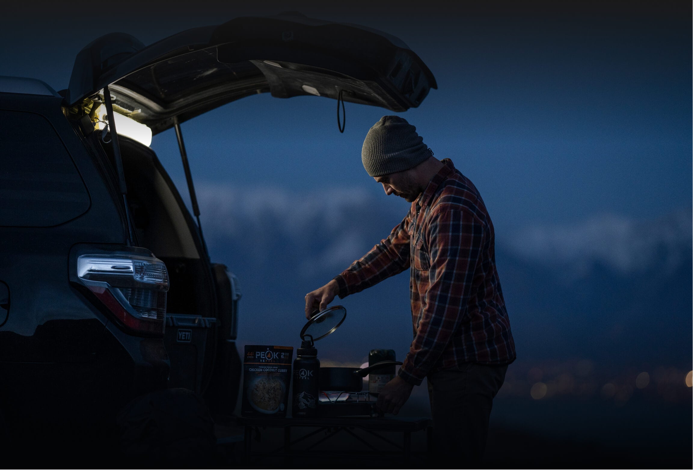 man camping at the car cooking on a camp stove