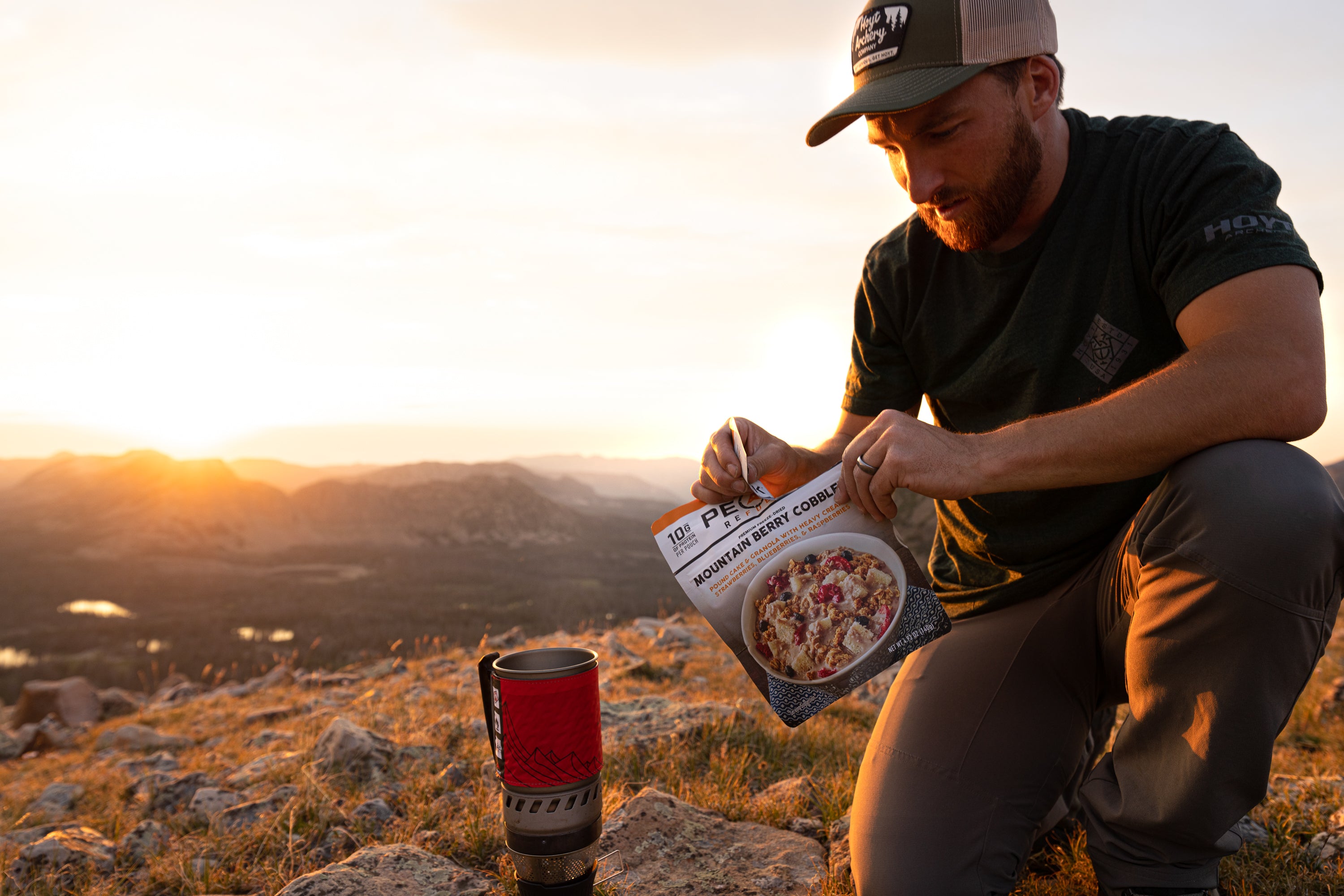 A man kneeling on a rocky hill enjoy a package of Mountain Berry Cobbler dessert.